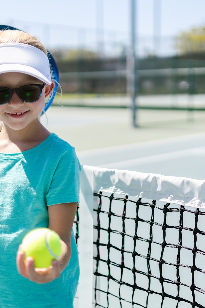 Smiling girl holding tennis racket and ball on a sunny tennis court.
